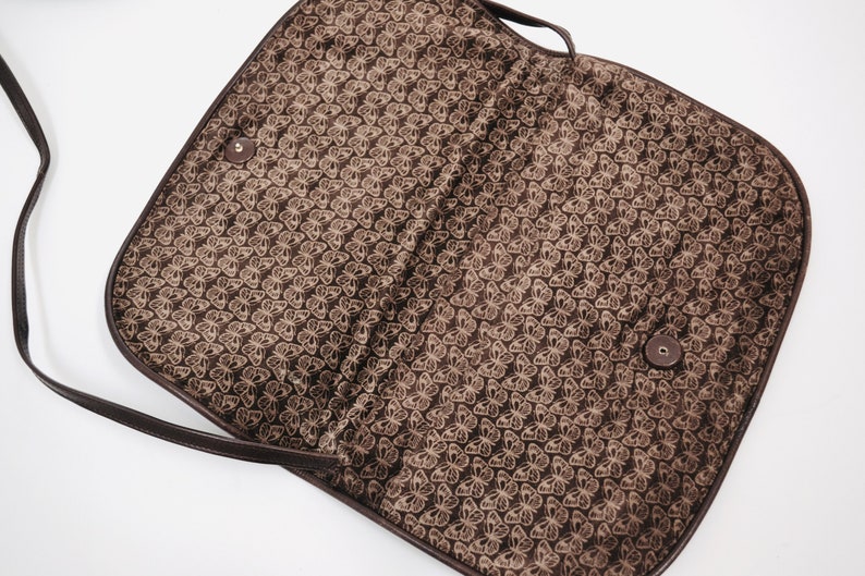 May include: A brown leather shoulder bag with a butterfly pattern lining. The bag has a flap closure and a long strap.
