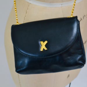 May include: A dark blue leather shoulder bag with a gold chain strap and a gold 'X' logo on the front.