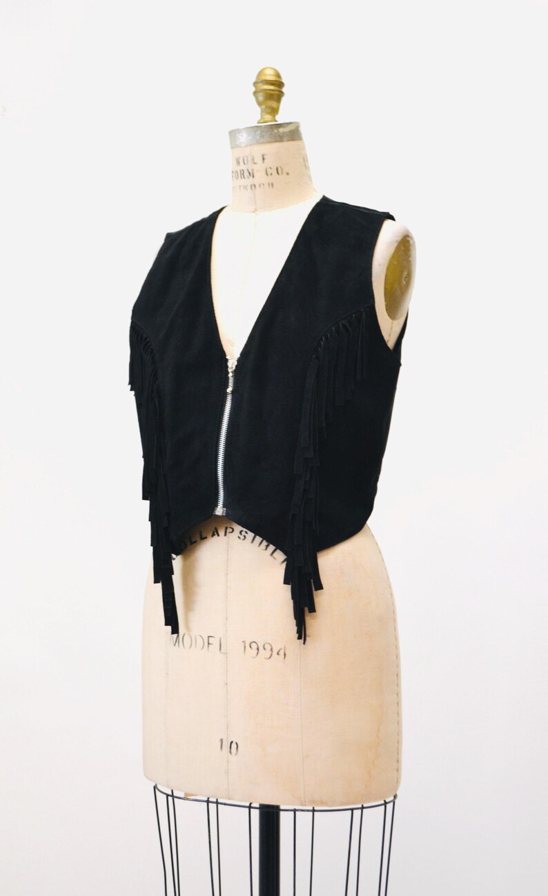May include: A black suede vest with fringe detailing and a zipper closure.