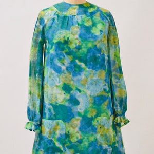 May include: A vintage 1960s tie-dye mini dress with long sleeves and a round neckline. The dress features a blue, green, and yellow tie-dye pattern. The dress has two pockets on the front and a ruffle trim on the sleeves.