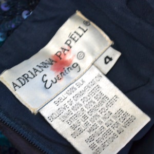 May include: A white tag with black text that reads "ADRIANNA PAPELL Evening" and a size 4. The tag is attached to a dark blue fabric.