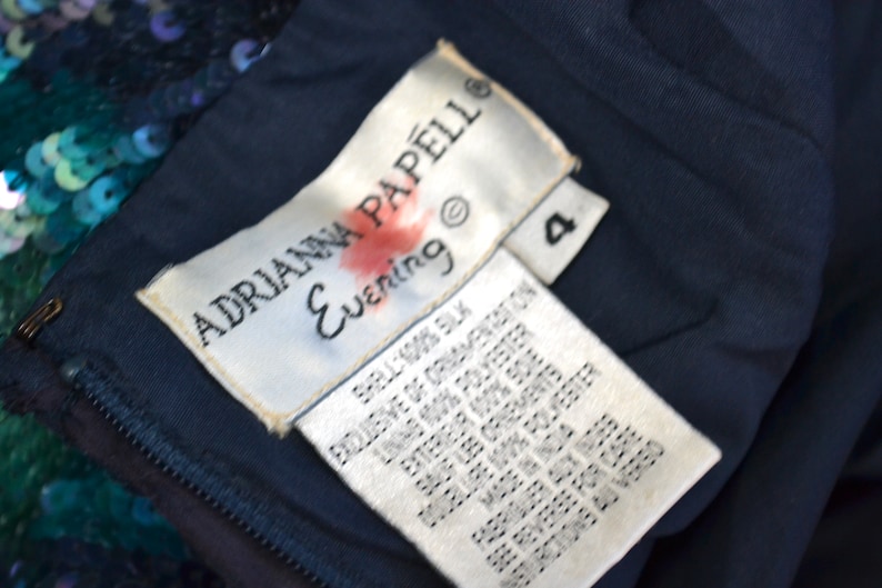 May include: A white tag with black text that reads "ADRIANNA PAPELL Evening" and a size 4. The tag is attached to a dark blue fabric.