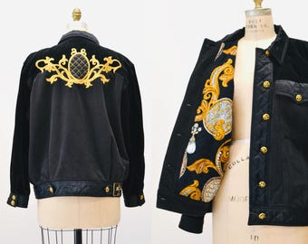 Puede incluir: Chaqueta de terciopelo negro con forro acolchado y bordados dorados en la espalda. El forro presenta un patrón de paisley con detalles dorados.
