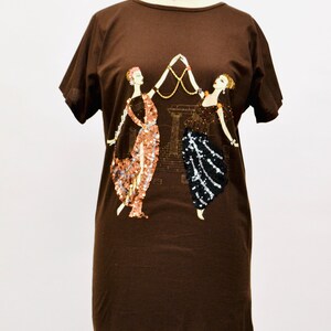May include: A brown t-shirt dress with an art deco design of two women holding a gold necklace. One woman's dress is embellished with copper sequins, the other with black sequins.