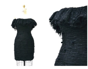 Puede incluir: Un vestido negro de hombros descubiertos con estampado de lunares y un escote con volantes. El vestido está hecho de una tela transparente y tiene una silueta ajustada.