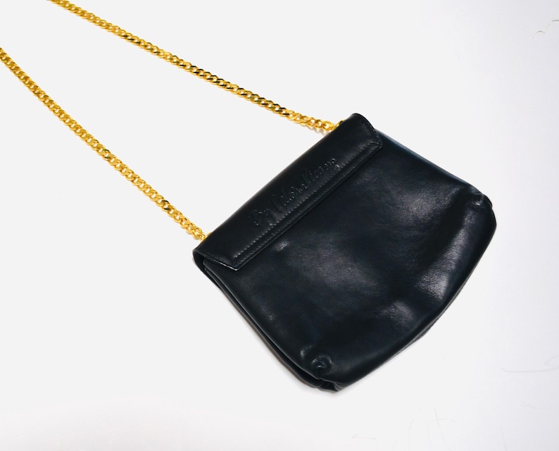 May include: A black leather shoulder bag with a gold chain strap. The bag has a flap closure and the brand name is embossed on the front.