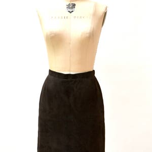 May include: A brown suede skirt on a dress form. The skirt is knee-length and has a straight silhouette.