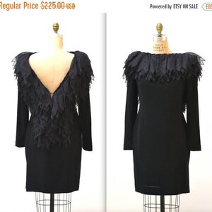 May include: A black dress with long sleeves and a ruffled neckline. The back of the dress features a large, layered ruffle.