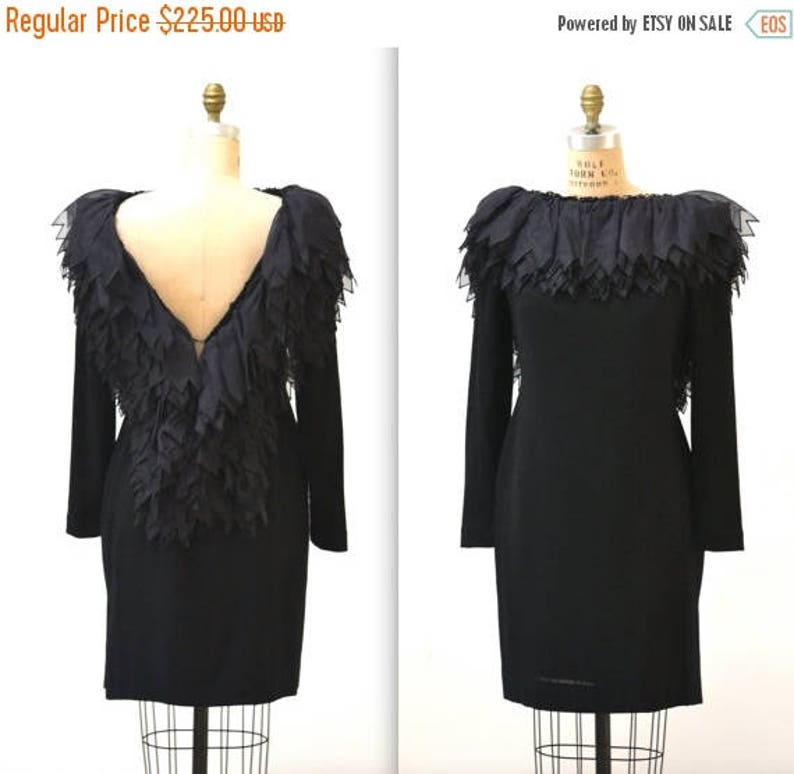 May include: A black dress with long sleeves and a ruffled neckline. The back of the dress features a large, layered ruffle.