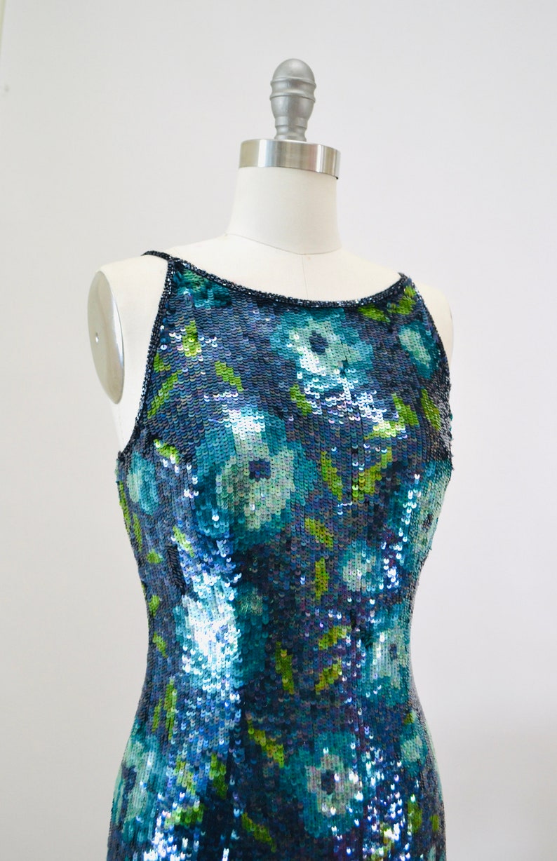 May include: A sleeveless sequined dress with a floral pattern in shades of blue, green, and white. The dress is fitted and has a scoop neckline.