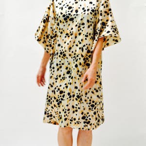 May include: A woman wearing a beige and black animal print dress with short sleeves. She is wearing black sandals with silver embellishments.