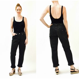 May include: A woman is wearing black high-waisted jeans with a cuffed hem and a black tank top. She is wearing sandals with a platform.