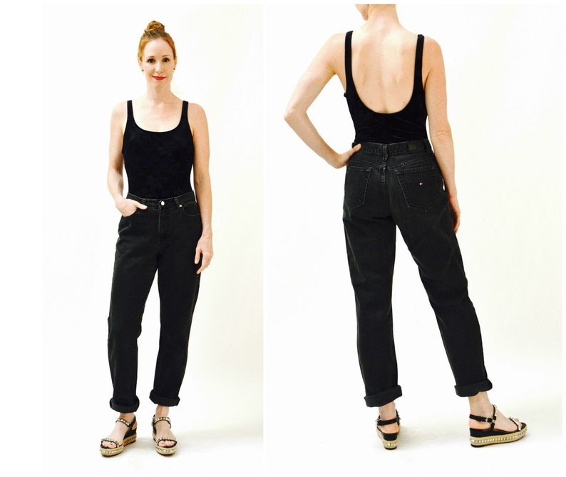 May include: A woman is wearing black high-waisted jeans with a cuffed hem and a black tank top. She is wearing sandals with a platform.