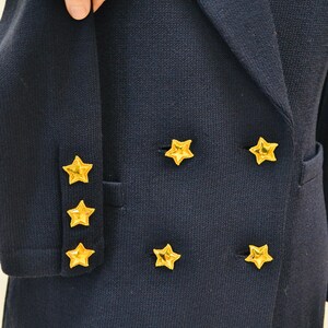 May include: A navy blue blazer with gold star buttons. The blazer has a double-breasted closure and a pocket on the left side.