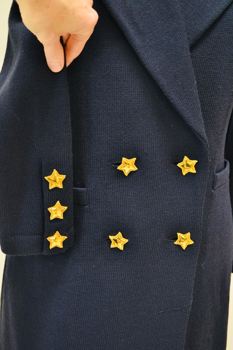May include: A navy blue blazer with gold star buttons. The blazer has a double-breasted closure and a pocket on the left side.