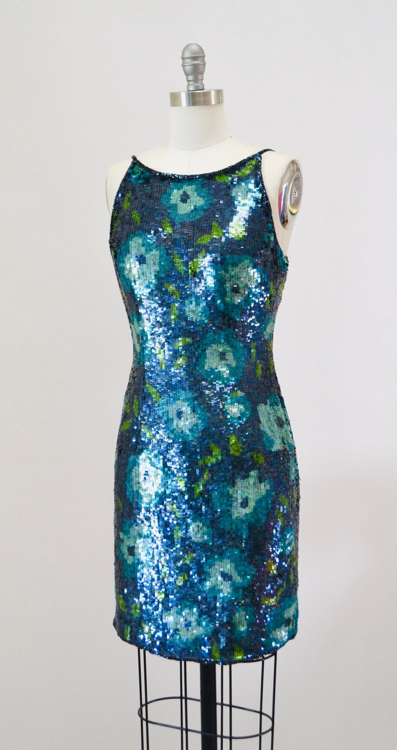 May include: A sleeveless sequined dress with a floral pattern in shades of blue and green.