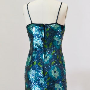 May include: A blue and green sequined mini dress with a floral pattern. The dress has thin straps and a back zipper.