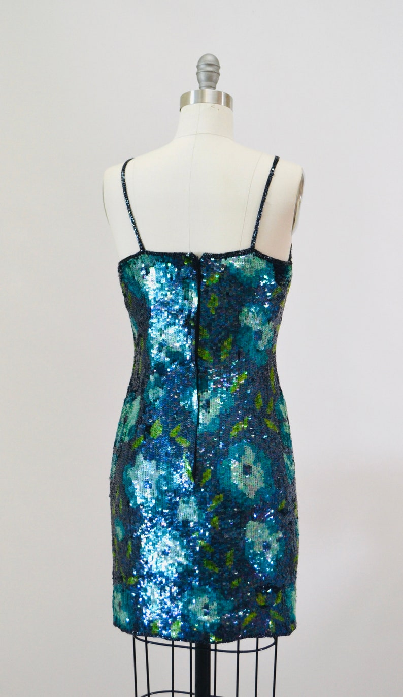 May include: A blue and green sequined mini dress with a floral pattern. The dress has thin straps and a back zipper.