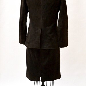 May include: A brown suede suit jacket and skirt set on a mannequin. The jacket has long sleeves and a classic cut. The skirt is knee-length and has a straight silhouette.