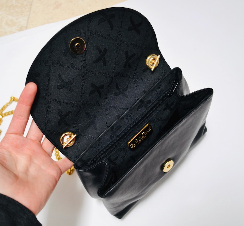 May include: Black leather handbag with a gold chain strap and a gold clasp. The inside of the bag is lined with black fabric and has a gold label that reads "Salvatore Ferragamo".