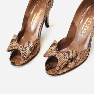 May include: A pair of brown and black snakeskin peep-toe heels with a bow detail. The shoes are made in Spain by the brand "La Martina".