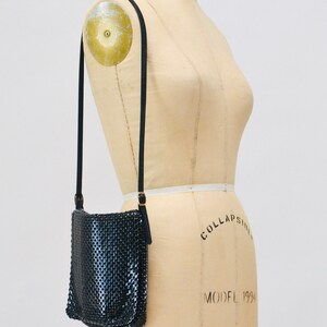 May include: A black mesh crossbody bag with a gold chain strap. The bag is hanging on a dress form.