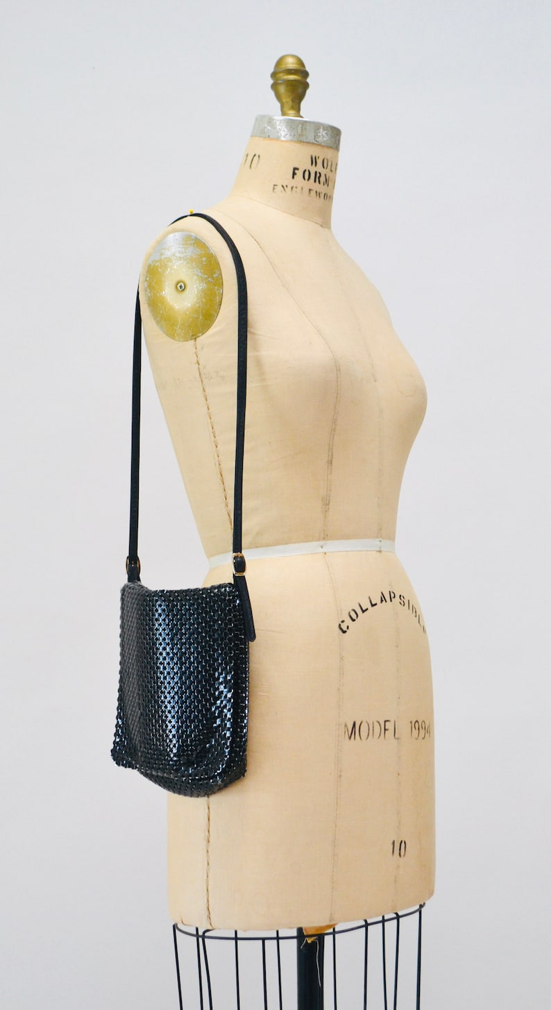 May include: A black mesh crossbody bag with a gold chain strap. The bag is hanging on a dress form.