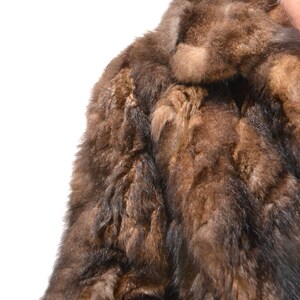May include: A brown fur coat with a long sleeve and a collar. The fur is soft and fluffy.