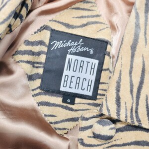 Op de afbeelding: Een bruin en zwart tijgerstreepjes su&egrave;de jack met een zwart label met de tekst "Michael Hoban" en "North Beach" met een maat 4 eronder gedrukt.