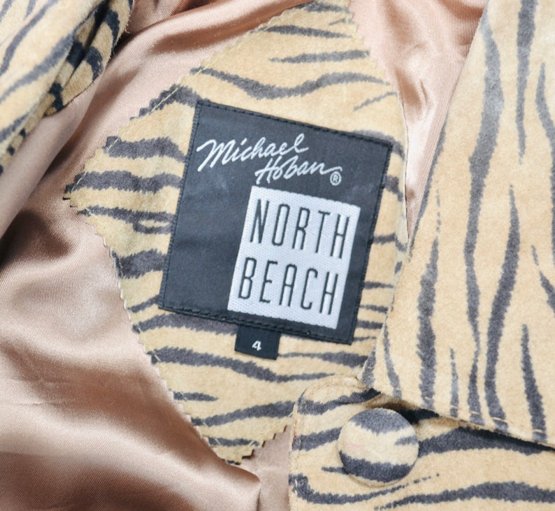 Op de afbeelding: Een bruin en zwart tijgerstreepjes su&egrave;de jack met een zwart label met de tekst "Michael Hoban" en "North Beach" met een maat 4 eronder gedrukt.