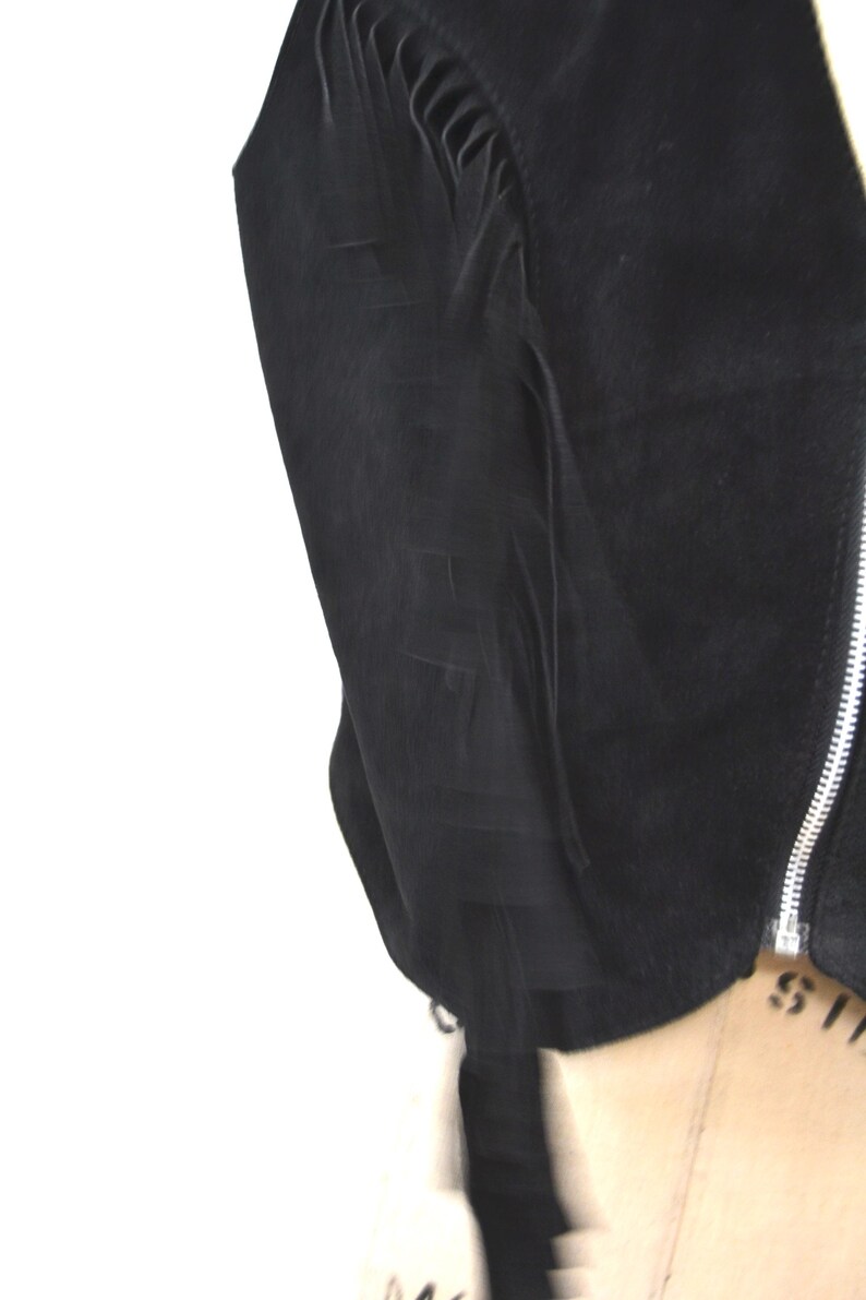 May include: Black suede jacket with a zipper closure and fringe detail on the sleeves.