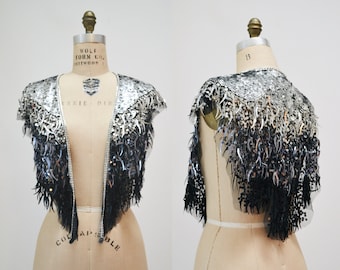 May include: A silver and black sequined shawl with fringe. The shawl is displayed on a dress form.