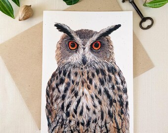 May include: A rectangular greeting card featuring a detailed painting of an owl with prominent ear tufts, striking orange eyes, and a plumage of brown, black, and cream feathers. The owl is depicted in a front-facing pose against a plain white background.