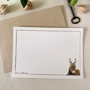 May include: A white card with a brown border and a small illustration of a donkey's head peeking out from the right side. The card has the text "Anna Johnson" printed in brown at the bottom.