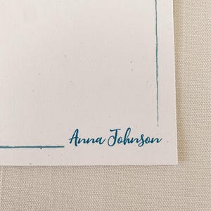 K&ouml;nnte beinhalten: Eine rechteckige, cremewei&szlig;e Karte mit einer d&uuml;nnen, blaugr&uuml;nen Randlinie entlang der rechten und unteren Kante. Der Name Anna Johnson ist in einer blaugr&uuml;nen Schreibschrift in der unteren rechten Ecke &uuml;ber der Randlinie aufgedruckt.