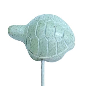 May include: A light green turtle garden stake with a textured shell and head. The turtle is mounted on a thin, silver metal rod, designed for placement in a garden or flower bed. The turtle's shell has a detailed, segmented pattern.