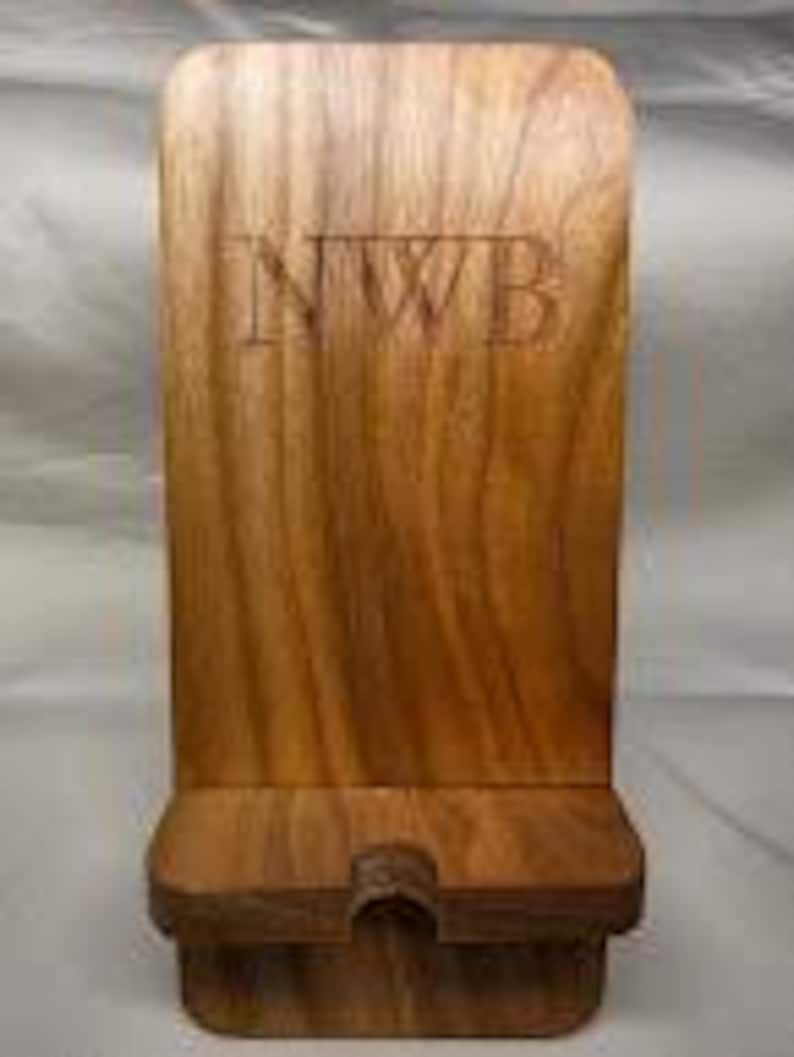 May include: A wooden phone stand with a rectangular back and a small base. The stand is made of a light brown wood and has the letters "NWB" carved into the front. The stand has a slot at the bottom to hold a phone.