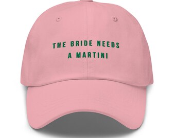 Puede incluir: Gorra de béisbol rosa claro con el texto verde "THE BRIDE NEEDS A MARTINI". La gorra tiene una visera curva y un cierre de correa ajustable. Un accesorio divertido para una despedida de soltera o evento nupcial.