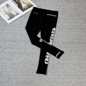 Puede incluir: Leggings negros con texto blanco "Chrome Hearts" en la pierna. Los leggings también presentan el logotipo "Chrome Hearts" en la parte delantera y trasera. Los leggings están hechos de un material suave y elástico.