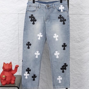 Könnte beinhalten: Hellblaue Jeans mit mehreren schwarzen und weißen Kreuzapplikationen. Die Jeans haben ein klassisches Fünf-Taschen-Design und eine gerade Beinpassform. Die Kreuze sind gleichmäßig über die Vorderseite der Jeans verteilt.