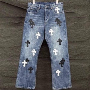 Könnte beinhalten: Blaue Jeans mit heller Waschung und mehreren Kreuzapplikationen in Schwarz und Weiß. Die Jeans haben ein klassisches Fünf-Taschen-Design und eine gerade Beinpassform. Die Kreuze sind gleichmäßig auf der Vorderseite der Jeans verteilt.