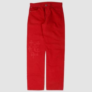 Könnte beinhalten: Leuchtend rote Jeans aus Denim mit klassischem Fünf-Taschen-Design. Die Jeans haben ein dekoratives Kreuzmuster auf dem linken Bein. Die Hose ist einfarbig und hat einen Knopf- und Reißverschluss.