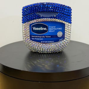Könnte beinhalten: Ein mit blauen und klaren Strasssteinen verziertes Glas Vaseline Original Protecting Jelly. Das Etikett zeigt "Vaseline" und "Dermatologically Tested Skin Protectant". Das Glas enthält 100 ml Produkt.