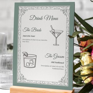 May include: A wedding drink menu with a green border and wooden base. The menu features the text "Drink Menu", "The Bride" with an Amaretto Sour illustration, and "The Groom" with an Old Fashioned illustration.