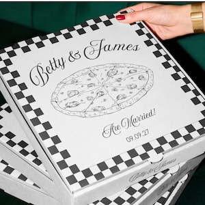 Könnte beinhalten: Ein weißer, quadratischer Pizzakarton mit einem schwarz karierten Rand. Der Deckel zeigt eine Strichzeichnung einer geschnittenen Pizza mit dem Text Betty & James Are Married! und dem Datum 09.09.27 in einer schwarzen Schriftkombination.