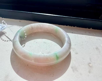 May include: A smooth, polished bangle bracelet crafted from translucent white stone with subtle, natural inclusions of vibrant green throughout the circular band. The material has a glossy, reflective surface that catches the light.