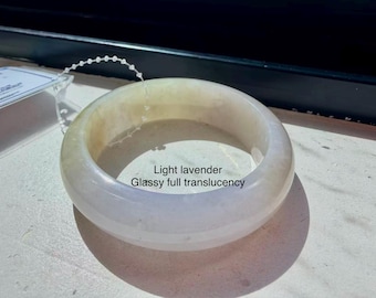 May include: A light lavender bangle bracelet with a smooth, rounded surface and glassy full translucency. The bracelet features a thin, clear plastic string attached to the top edge and includes the text Light lavender Glassy full translucency.