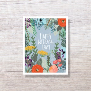 May include: A greeting card with a floral design and the text "Happy Wedding Day!". The card features a light blue background with colorful flowers in shades of orange, yellow, pink, and blue, surrounded by green foliage.