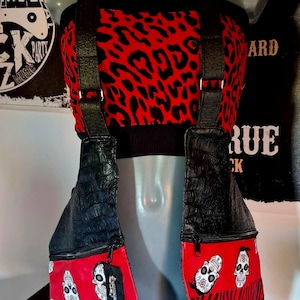 Puede incluir: Un bolso bandolera rojo y negro con un top a juego. El bolso presenta cuero negro con textura de cocodrilo y paneles rojos con diseños de calaveras blancas. El top tiene un estampado de leopardo rojo.