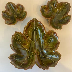 May include: Set of three ceramic leaf-shaped serving dishes. The dishes are glazed in shades of green and brown, with detailed veining. The set includes one large dish and two smaller ones, all with a glossy finish. Ideal for serving snacks or as decorative pieces.